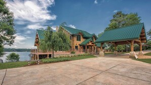 A large log cabin with a green roof, a covered porch, and a view of a lake. - Azalea Retreat- The Lodge by Avantstay Best View (Sherrills Ford)