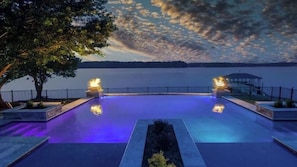 Piscina com duas tochas, rodeada por um deck com vista para um lago e montanhas.