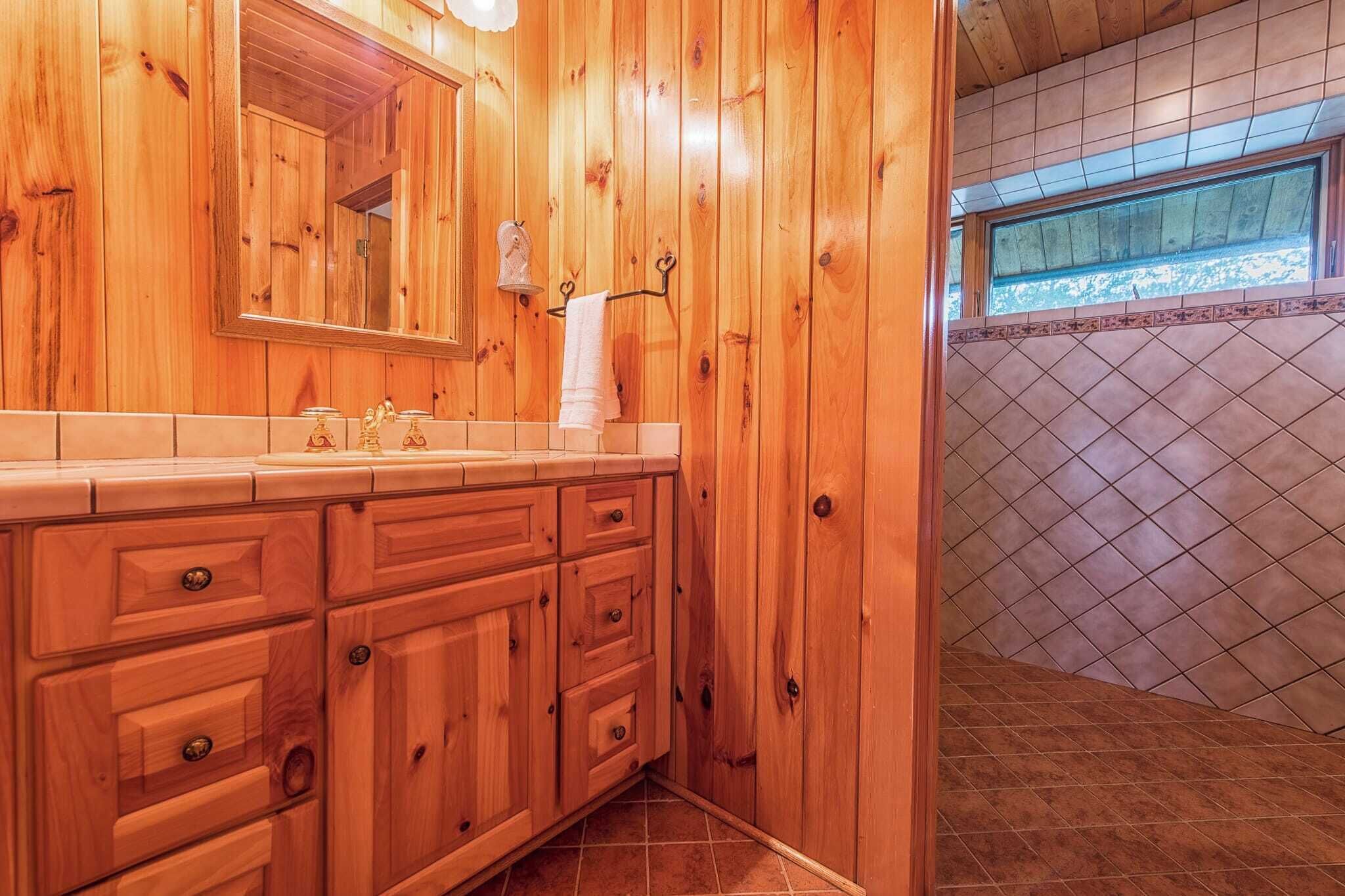 A wooden bathroom with a large mirror, wooden cabinets, and a tiled floor.