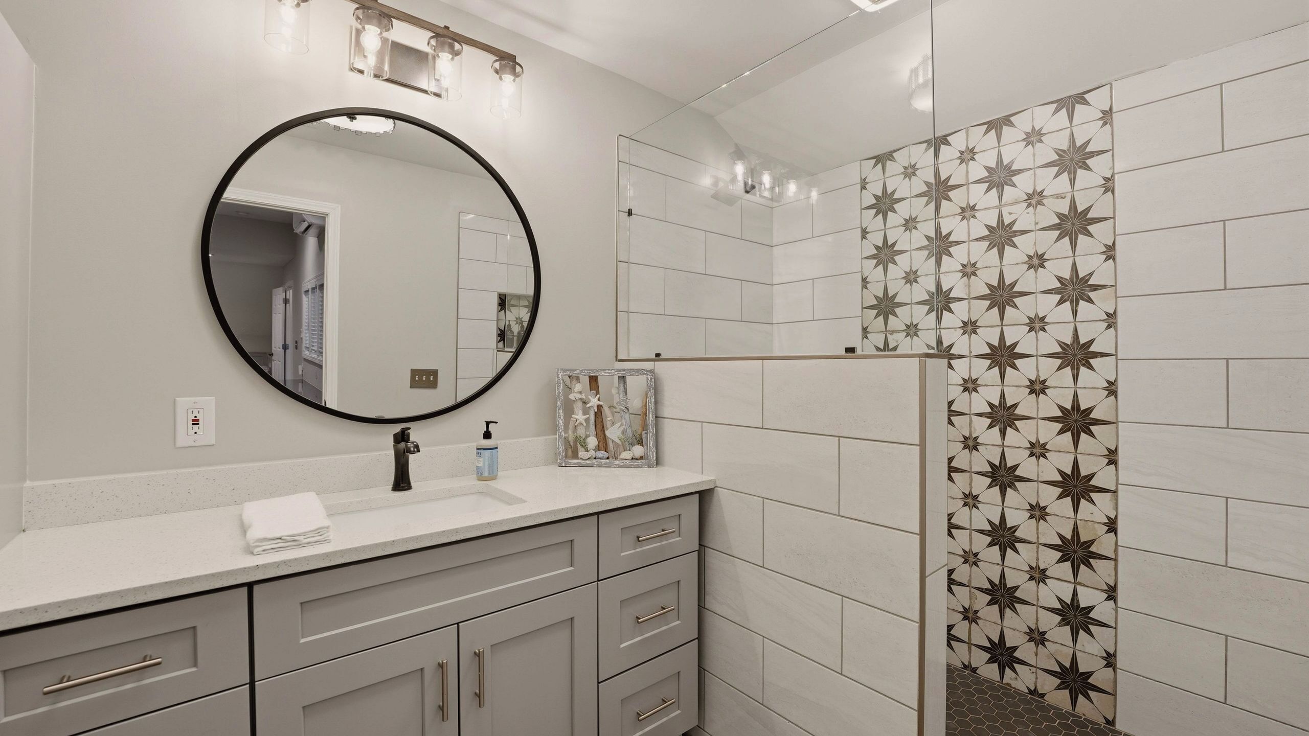 Une salle de bain avec un miroir rond, un lavabo avec un robinet, un tableau encadré et des murs carrelés.