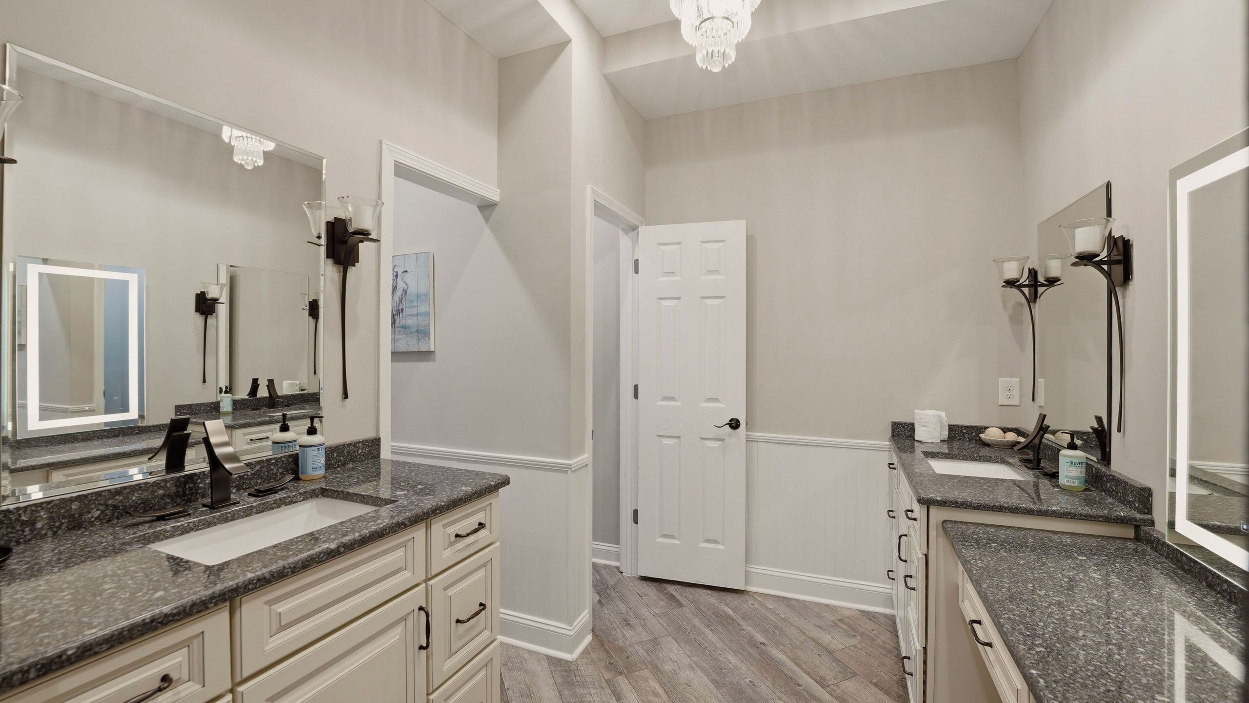 A bathroom with two sinks, a large mirror, and a door leading to another room.