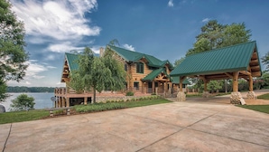A large log cabin with a green roof, a covered porch, and a view of a lake. - Azalea Retreat by Avantstay Sleeps 34 & Pool (Sherrills Ford)