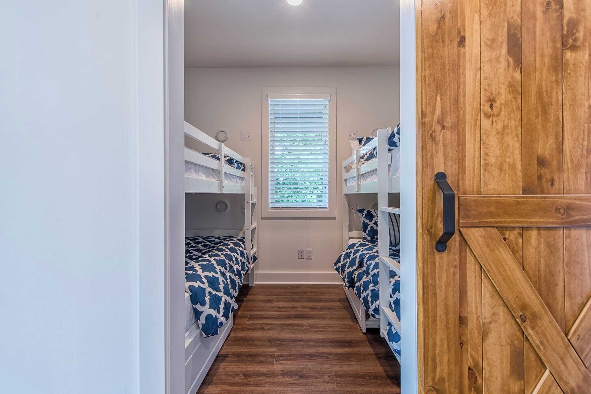A narrow hallway with bunk beds, a window with blinds, and a wooden door.