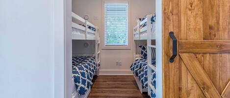 A narrow hallway with bunk beds, a window with blinds, and a wooden door.
