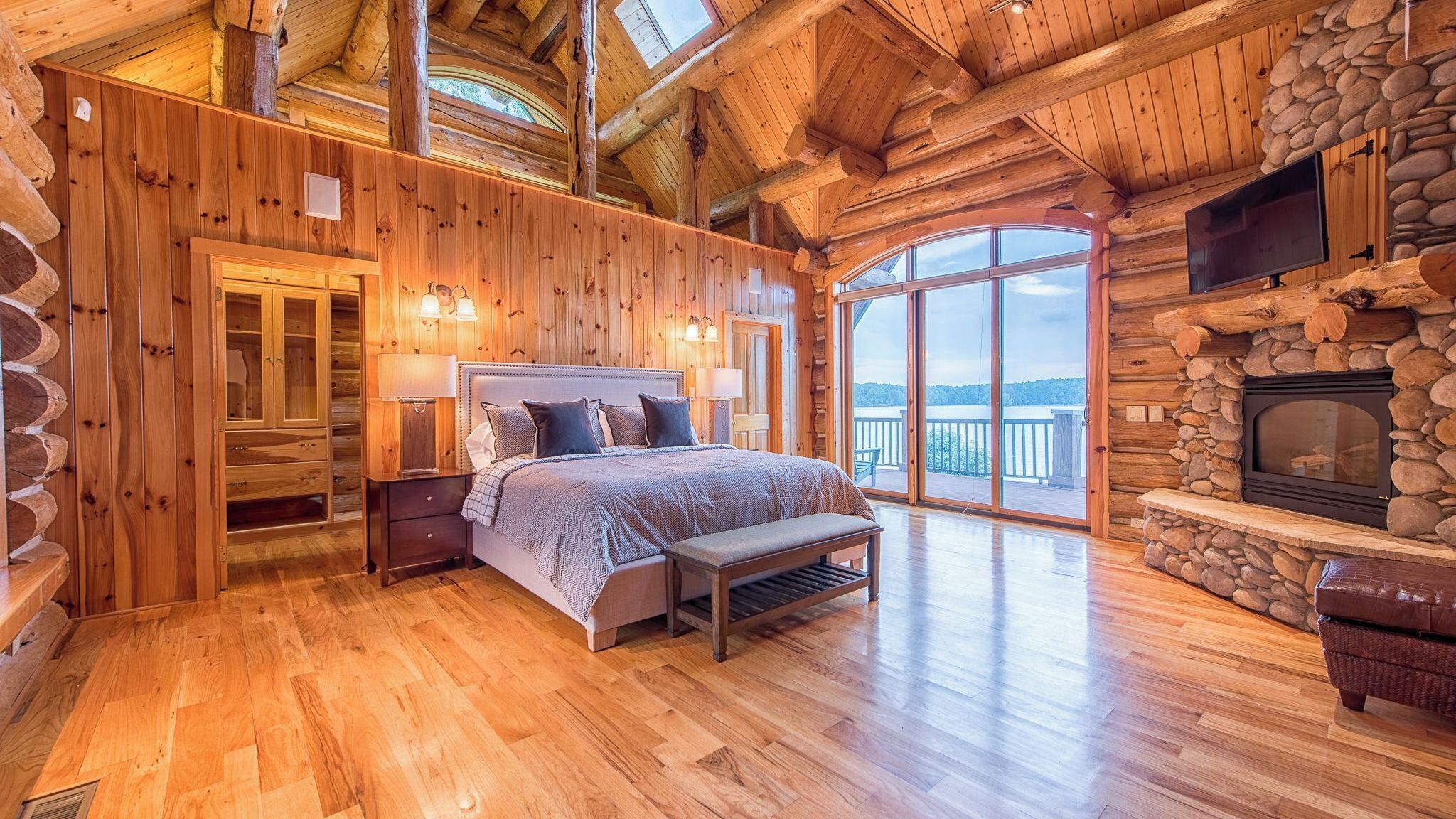 A log cabin bedroom with a bed, bench, and stone fireplace.