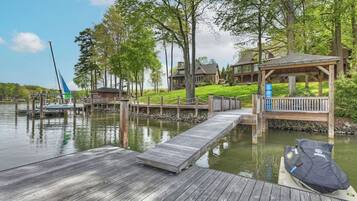 A lakeside property with a dock, a covered seating area, and a sailboat.