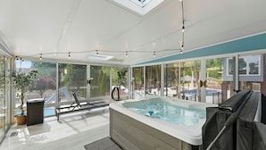 Una piscina interior moderna con recinto de cristal, una banca y un jacuzzi.