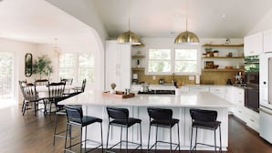 A modern kitchen with a large island, bar stools, pendant lighting, and a dining area with a table and chairs. - Hummingbird Home by Avantstay Hot tub + Sauna (Statesville)