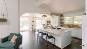 A modern kitchen with a large island, bar stools, pendant lighting, and a view of the outdoors.