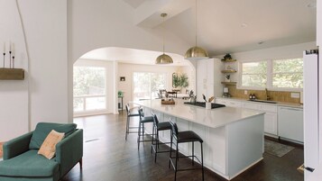 Una cocina moderna con una isla grande, taburetes de bar, iluminación colgante y vistas al exterior.