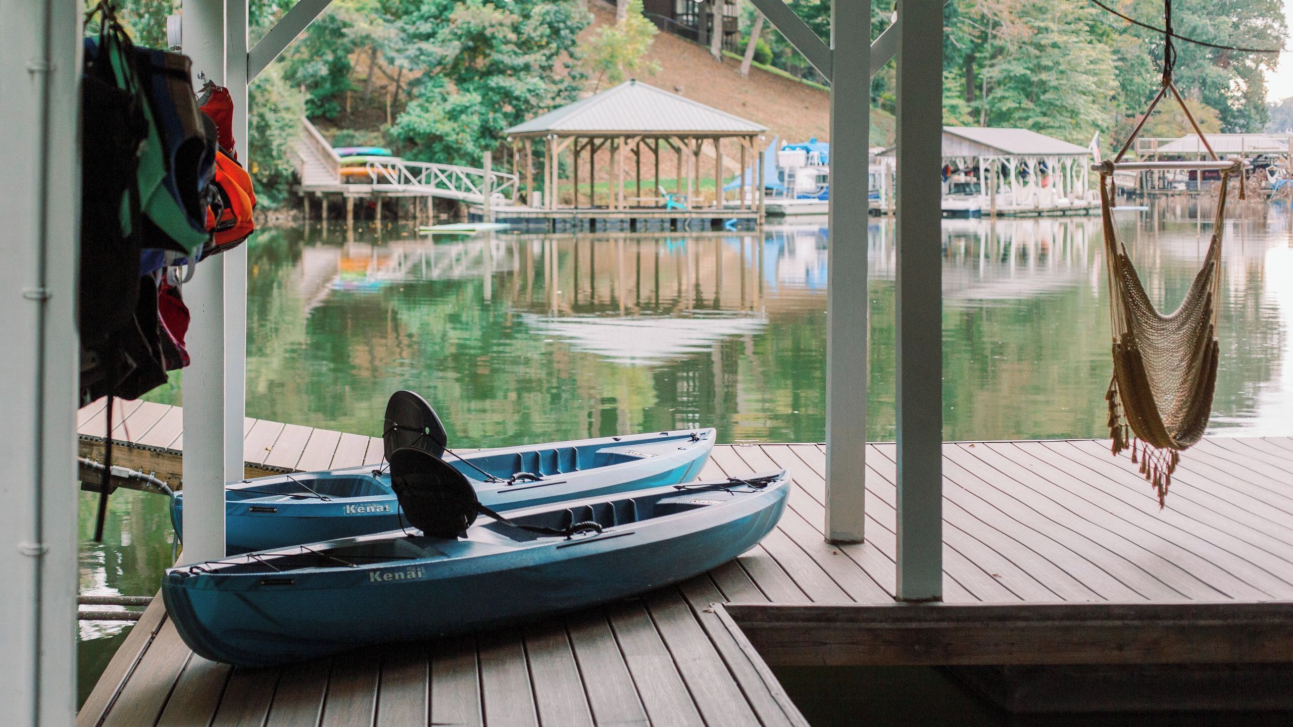 A dock with a blue canoe, a hammock, and a gazebo in the background.