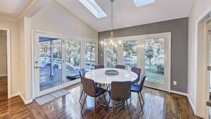 A dining area with a round table, six chairs, and a chandelier. There are large windows with a view of a deck and trees. - Lakefront Home Private Dock, Tiki Bar, Firepit Shore to Please by Avantstay (Denver)