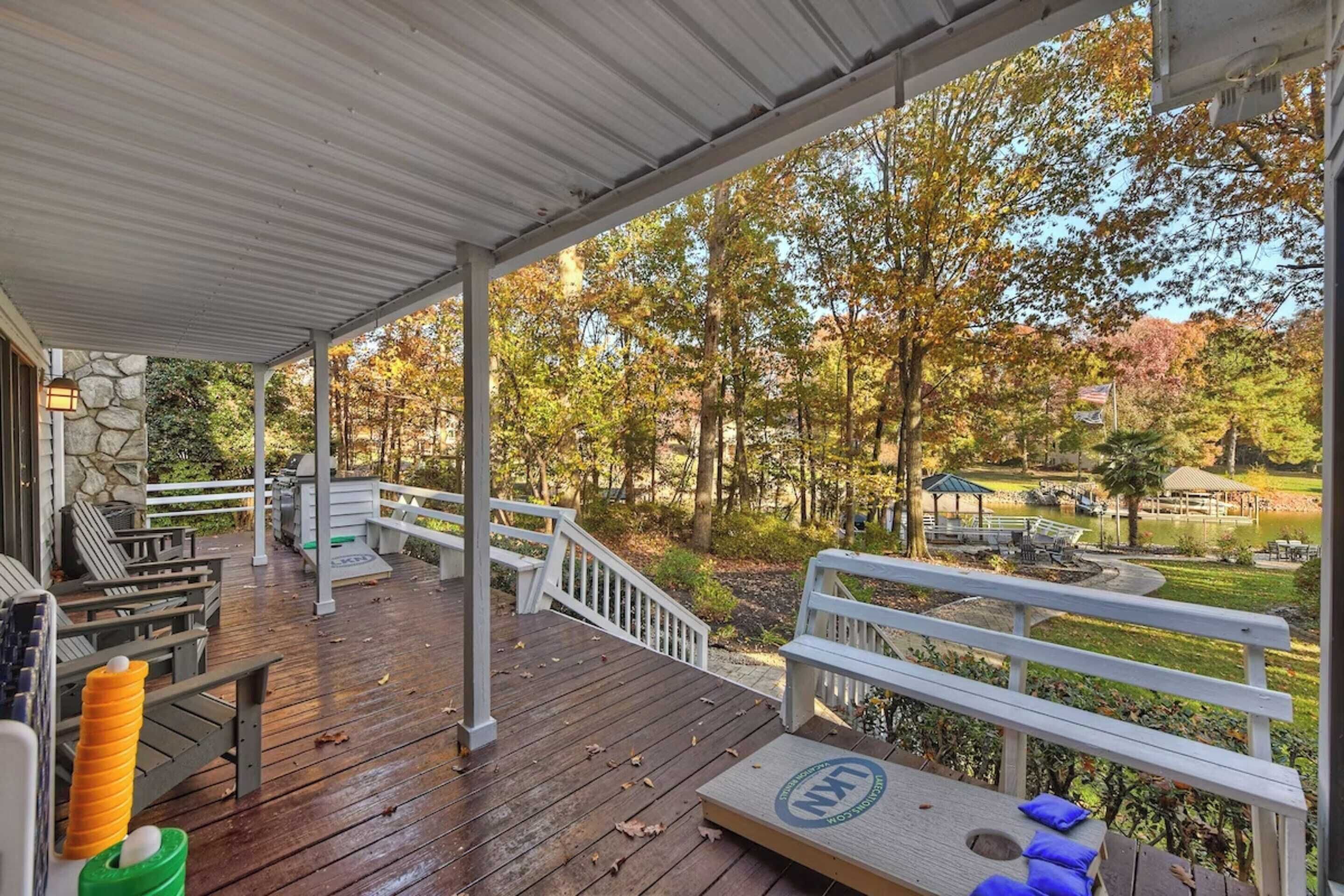 A covered outdoor deck with wooden flooring, white railings, and a stone wall.