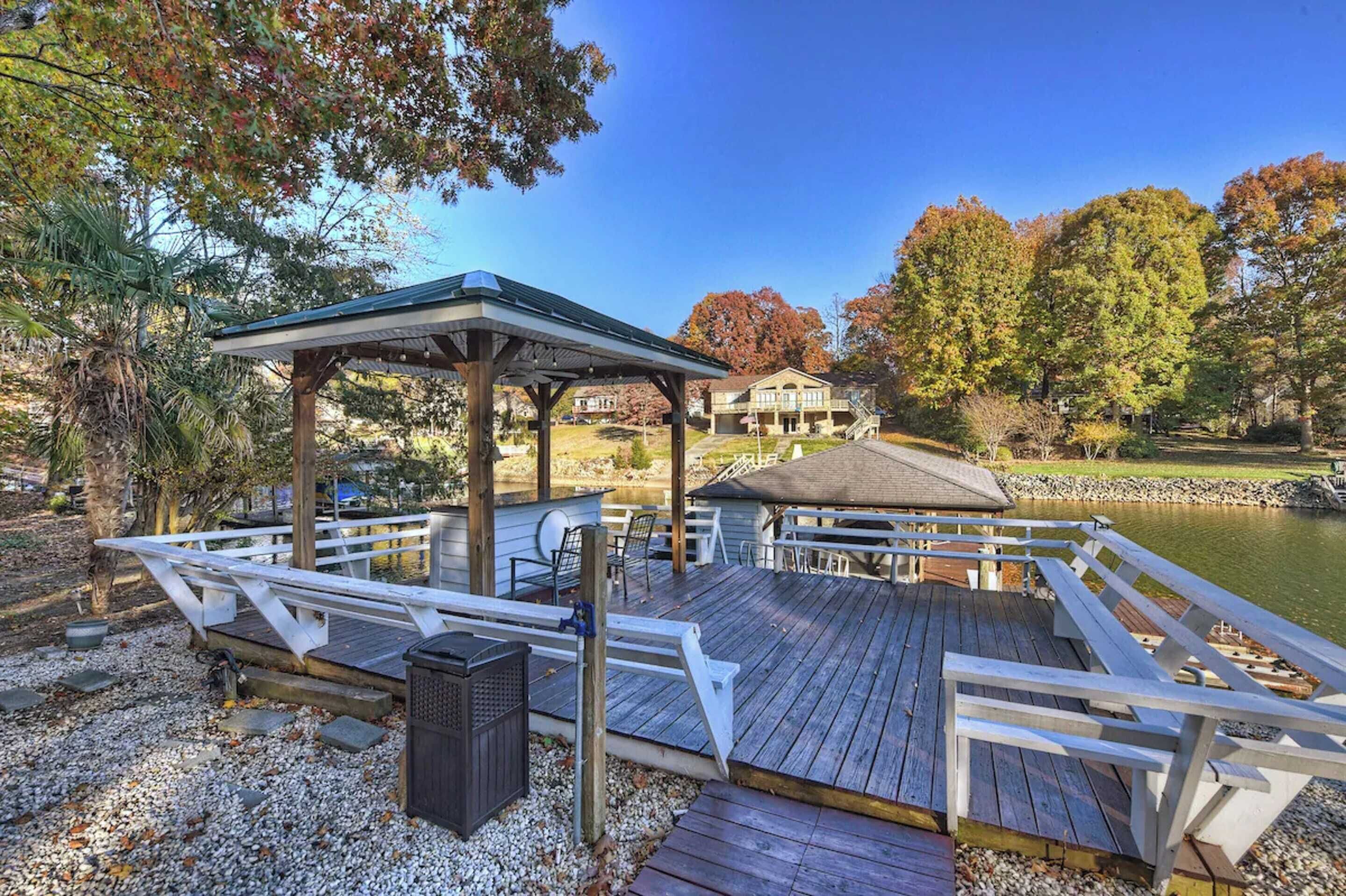 A wooden deck with a gazebo, outdoor seating, and a view of a lake and buildings in the background.