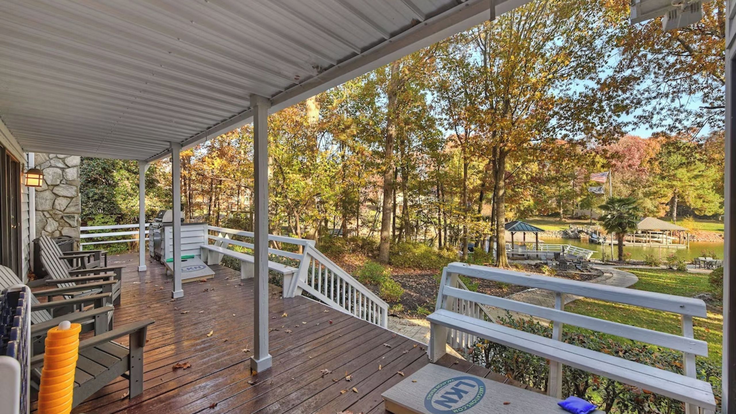 A covered deck with outdoor seating, a stone wall, and a view of a park with trees and a pond.