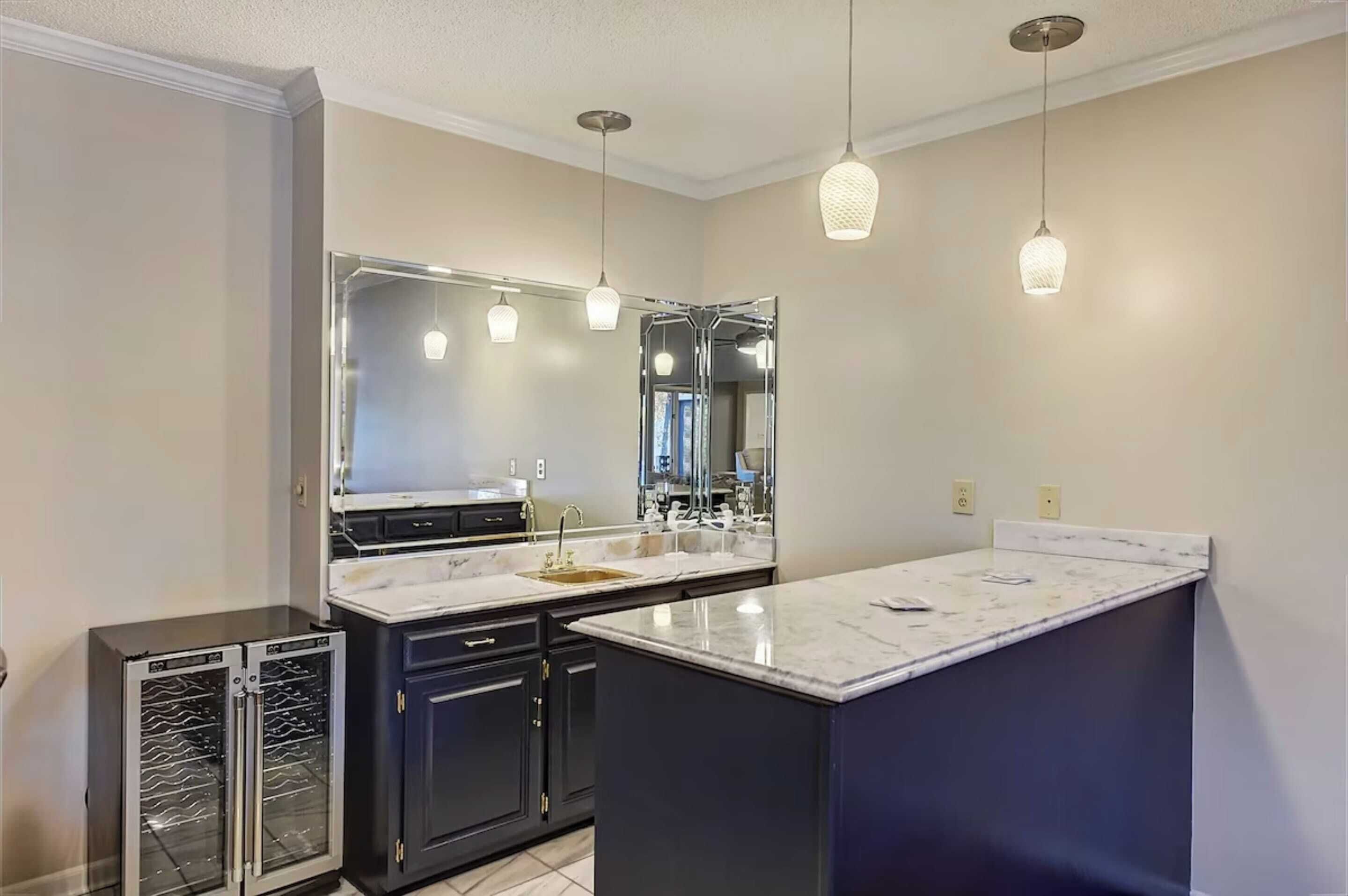 A modern kitchen with dark cabinets, a marble countertop, and pendant lighting.