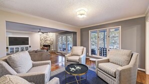 A living room with a stone fireplace, a ceiling fan, and a large window. - Lakefront Home Private Dock, Tiki Bar, Firepit Shore to Please by Avantstay (Denver)