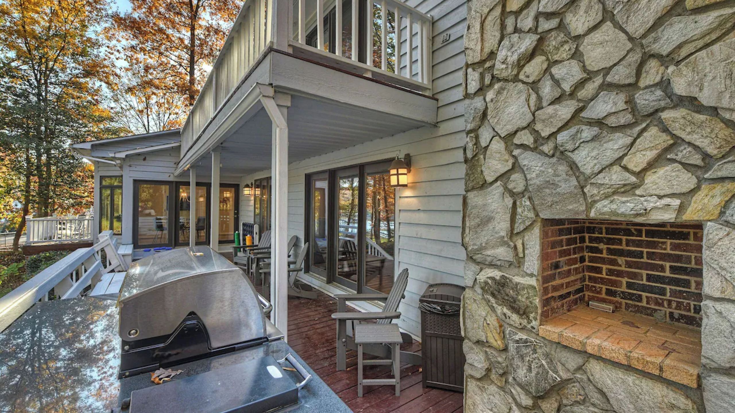 A covered outdoor area with a grill, seating, and a stone fireplace.