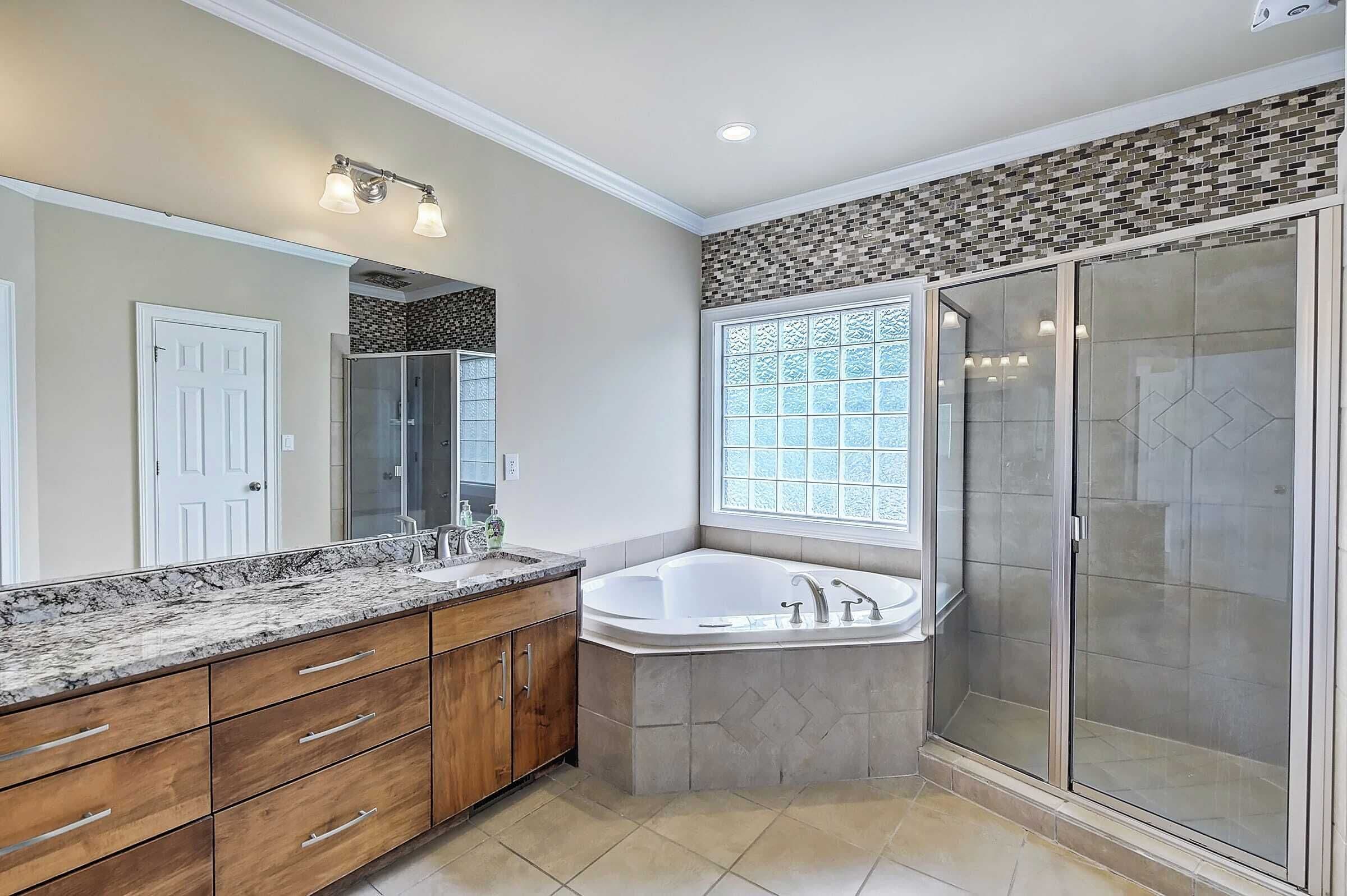 A modern bathroom with a large vanity, a freestanding bathtub, a glass shower enclosure, and a window providing natural light.