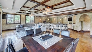 A spacious living area with a large dining table, a sofa set, and a kitchen in the background.
