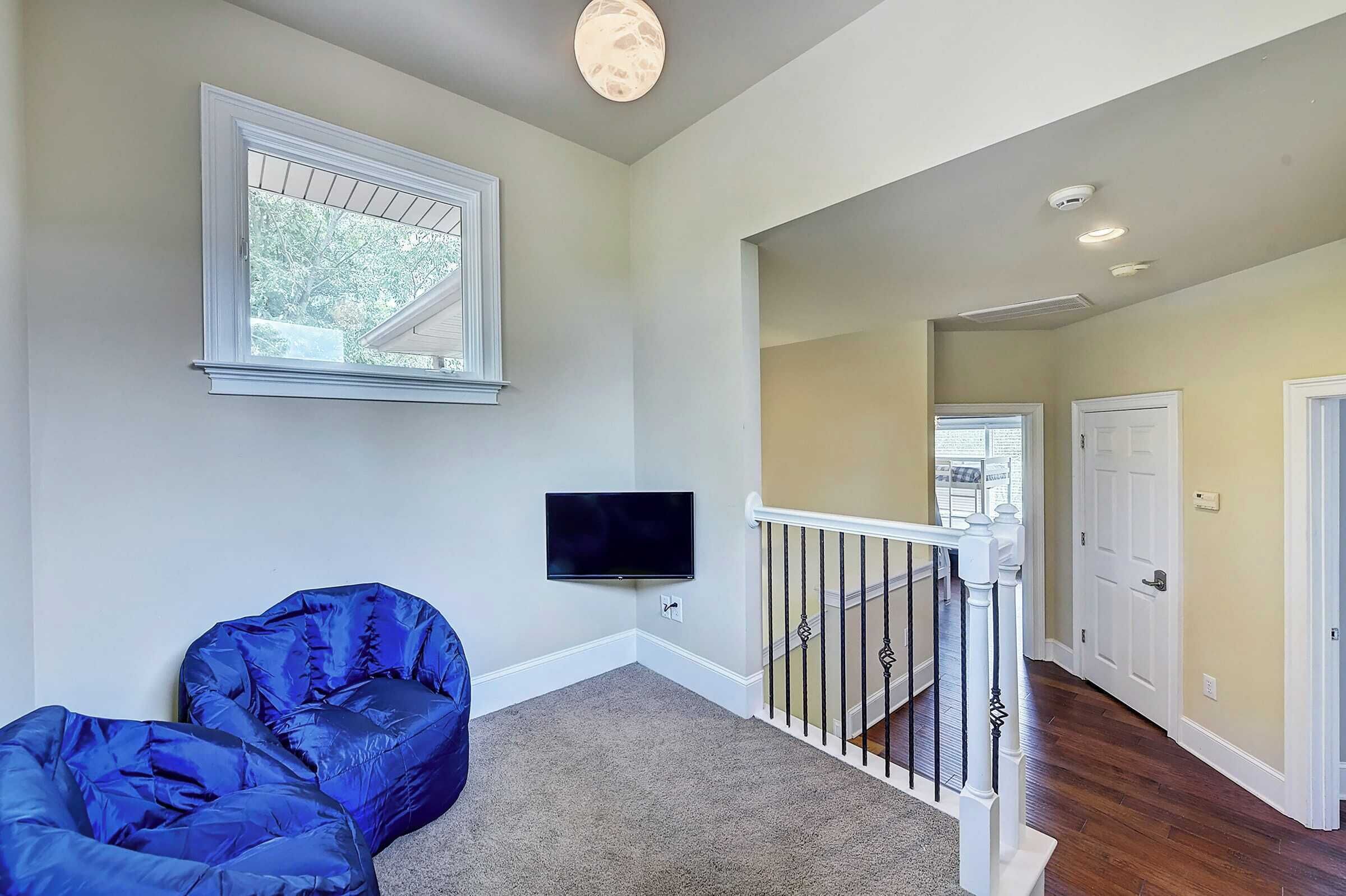 A room with a television mounted on the wall, a blue bean bag chair, and a staircase leading to another level.