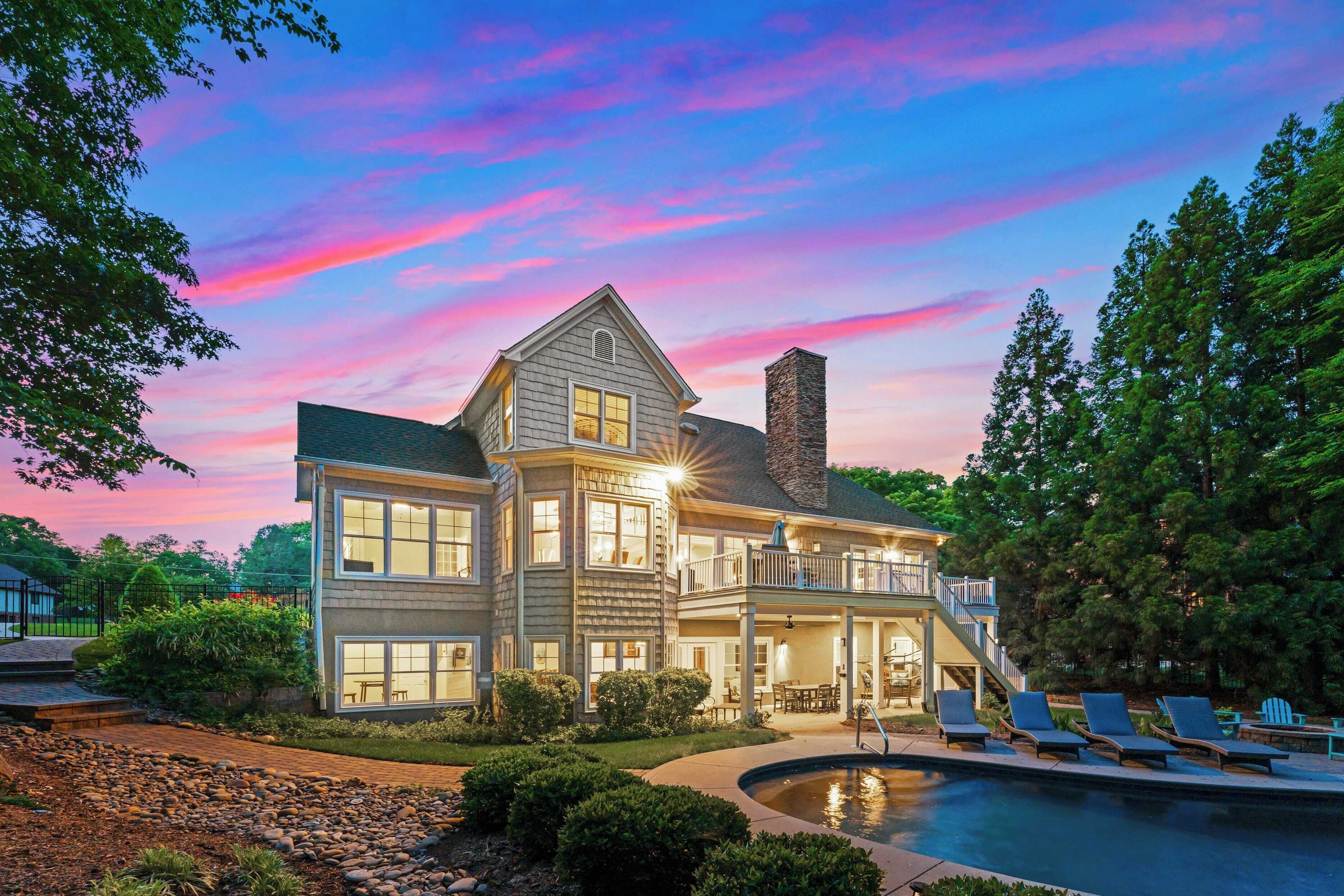 A large, two-story house with a pool and outdoor seating area, surrounded by trees and a well-maintained garden.