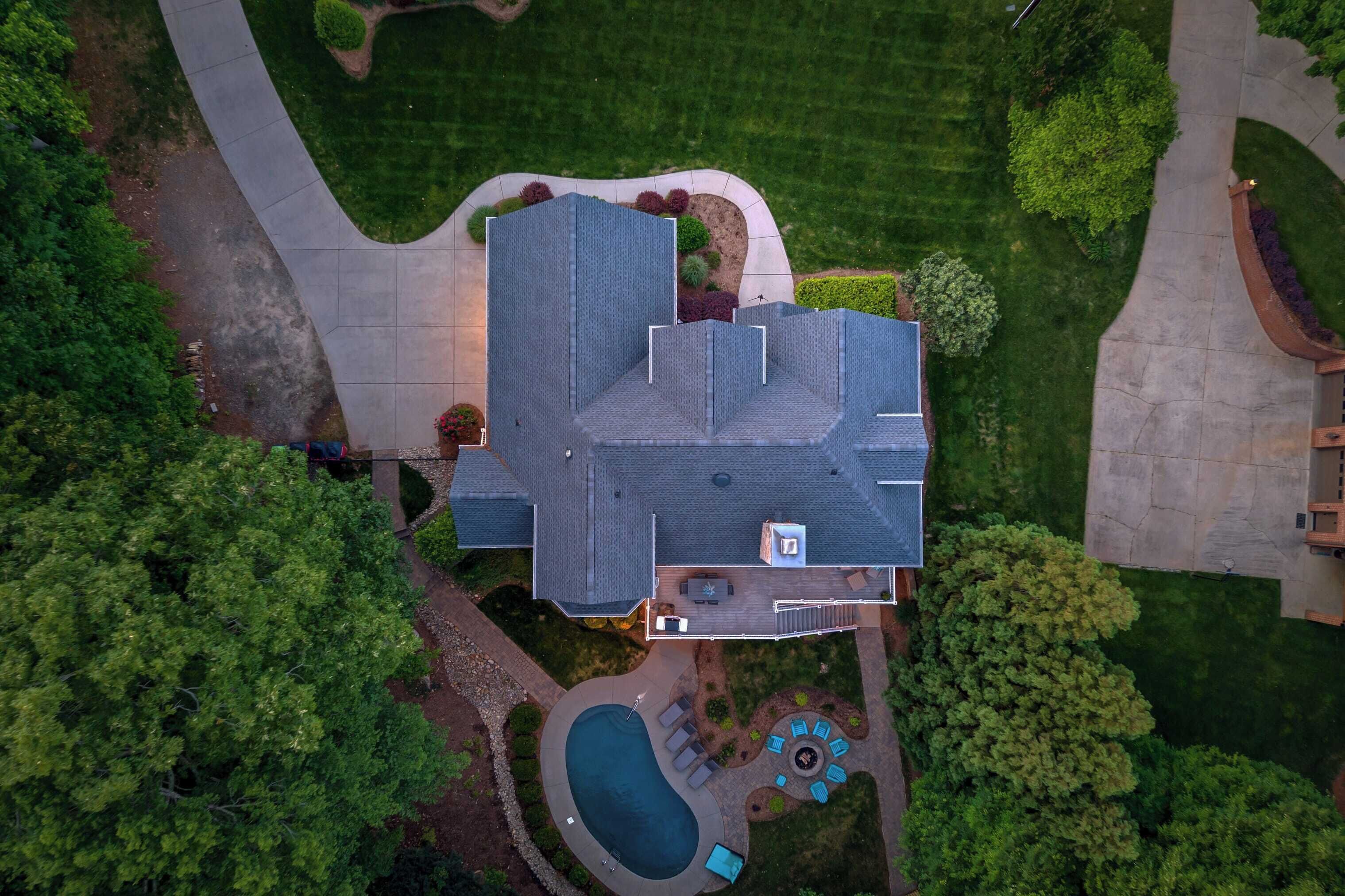 An aerial view of a house with a large deck, a swimming pool, and a well-maintained lawn.