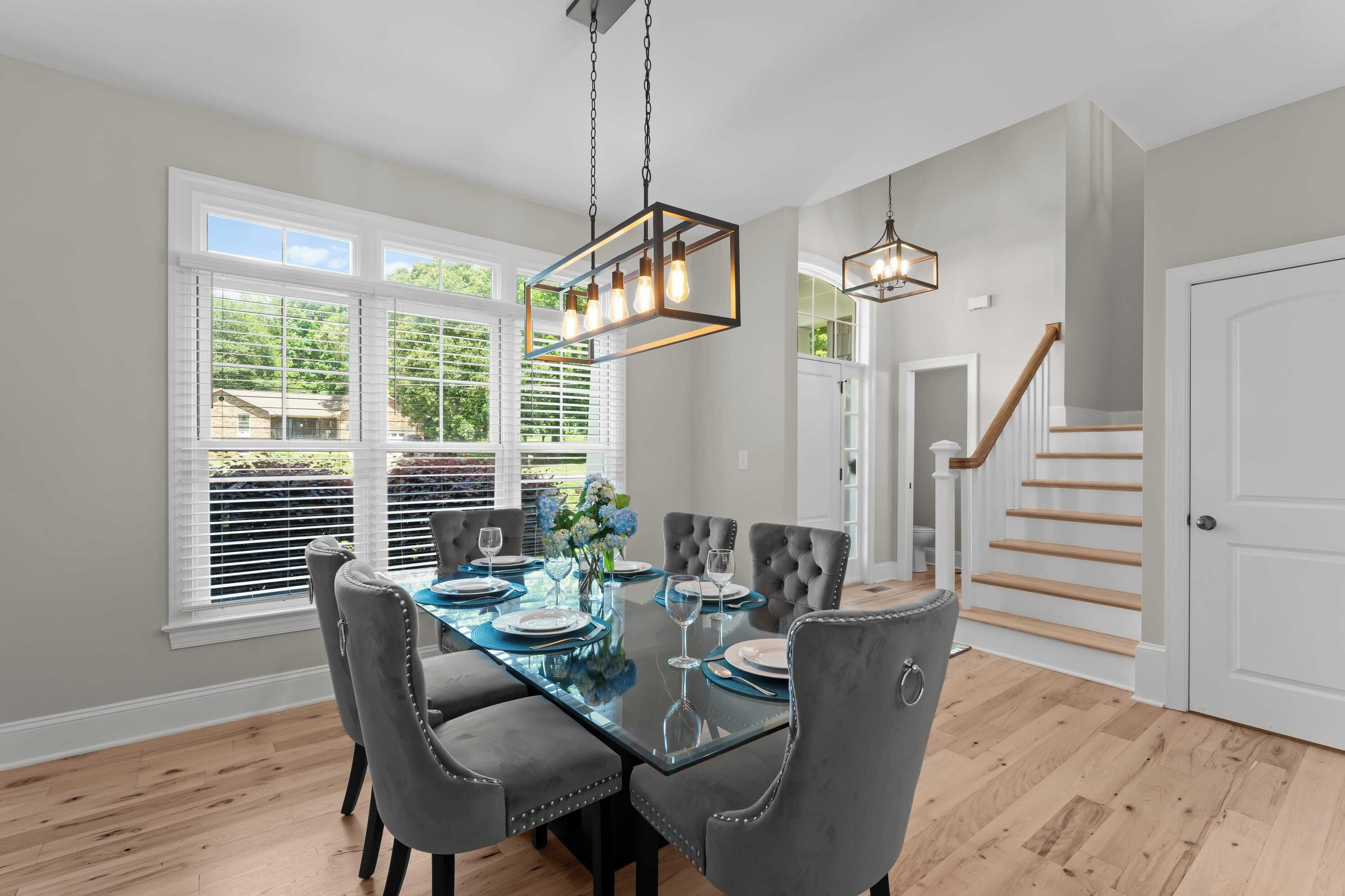 A dining area with a glass table, grey upholstered chairs, and pendant lighting.