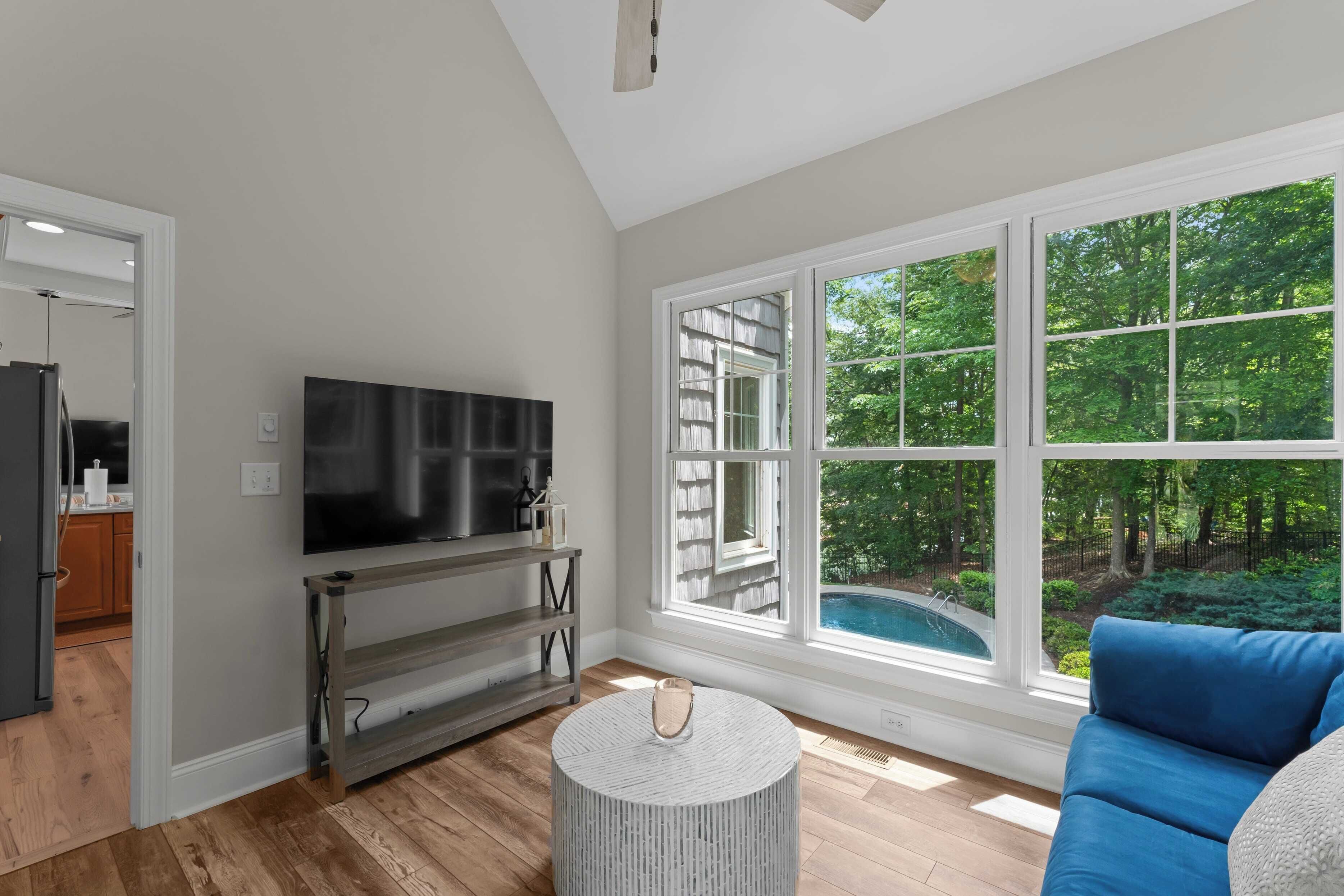 A modern living room with a large window, a flat-screen TV, a round coffee table, and a blue sofa.