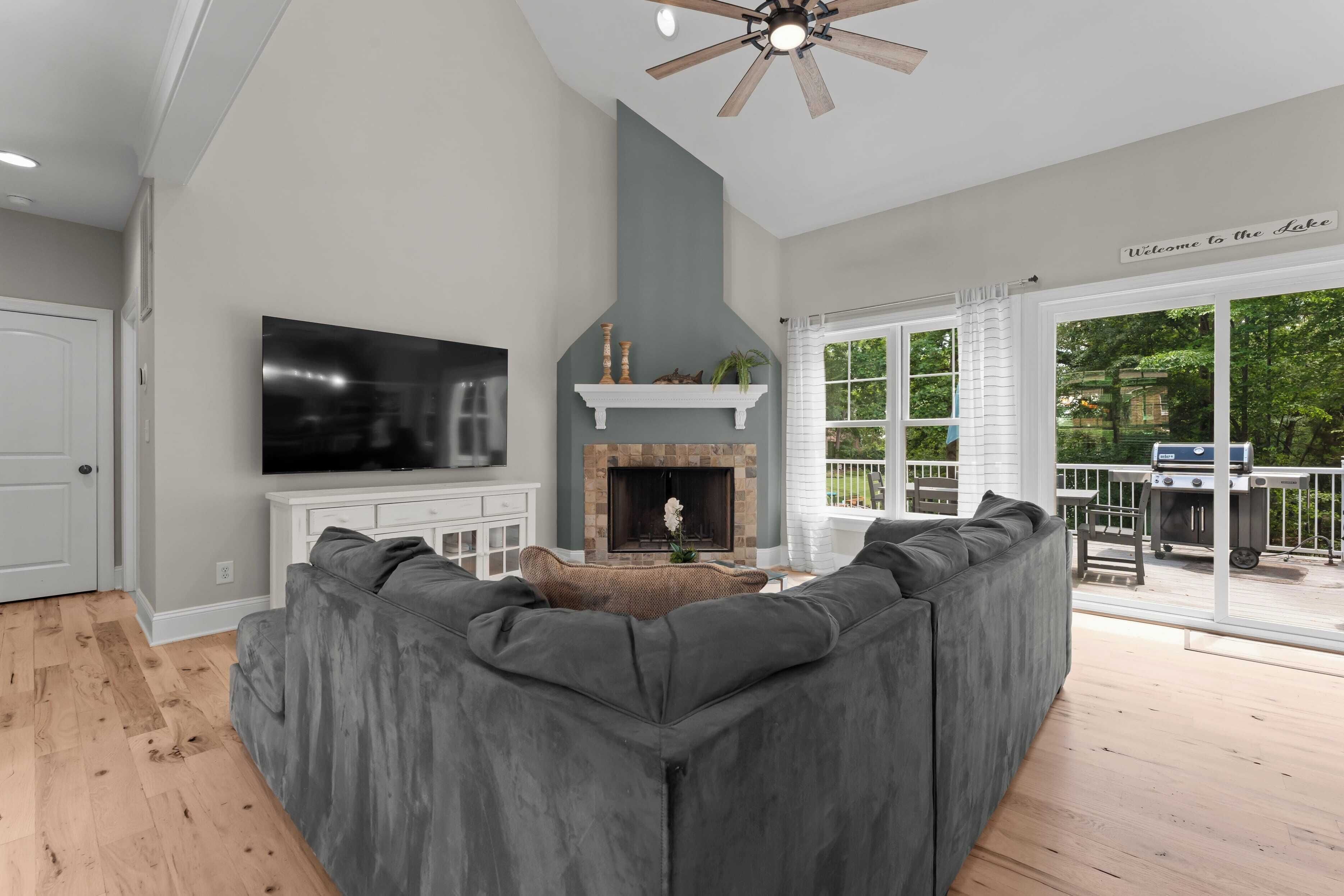 A modern living room with a gray sectional sofa, a flat-screen TV, a fireplace, and a ceiling fan.