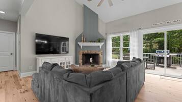 A modern living room with a gray sectional sofa, a flat-screen TV, a fireplace, and a ceiling fan.