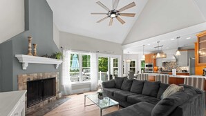 A spacious living room with a fireplace, a large gray sectional sofa, and a glass coffee table. - Making Waves by Avantstay Sleeps 20 + Pool (Denver)
