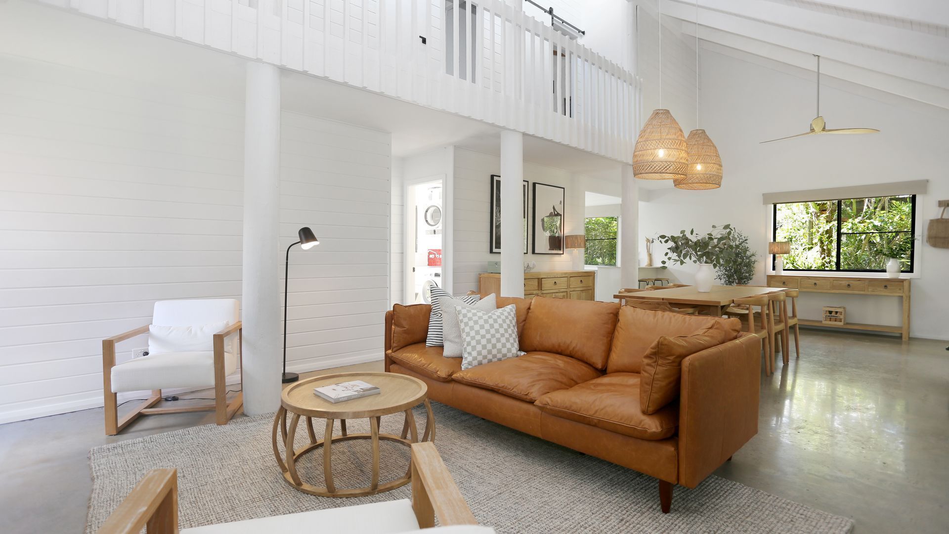 A spacious living area with a leather sofa, a round wooden coffee table, and a white armchair. A dining area with a wooden table and chairs is visible in the background.