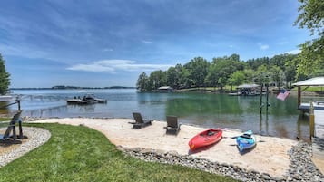A lakeside deck with kayaks, a dock, and a grassy area with chairs.
