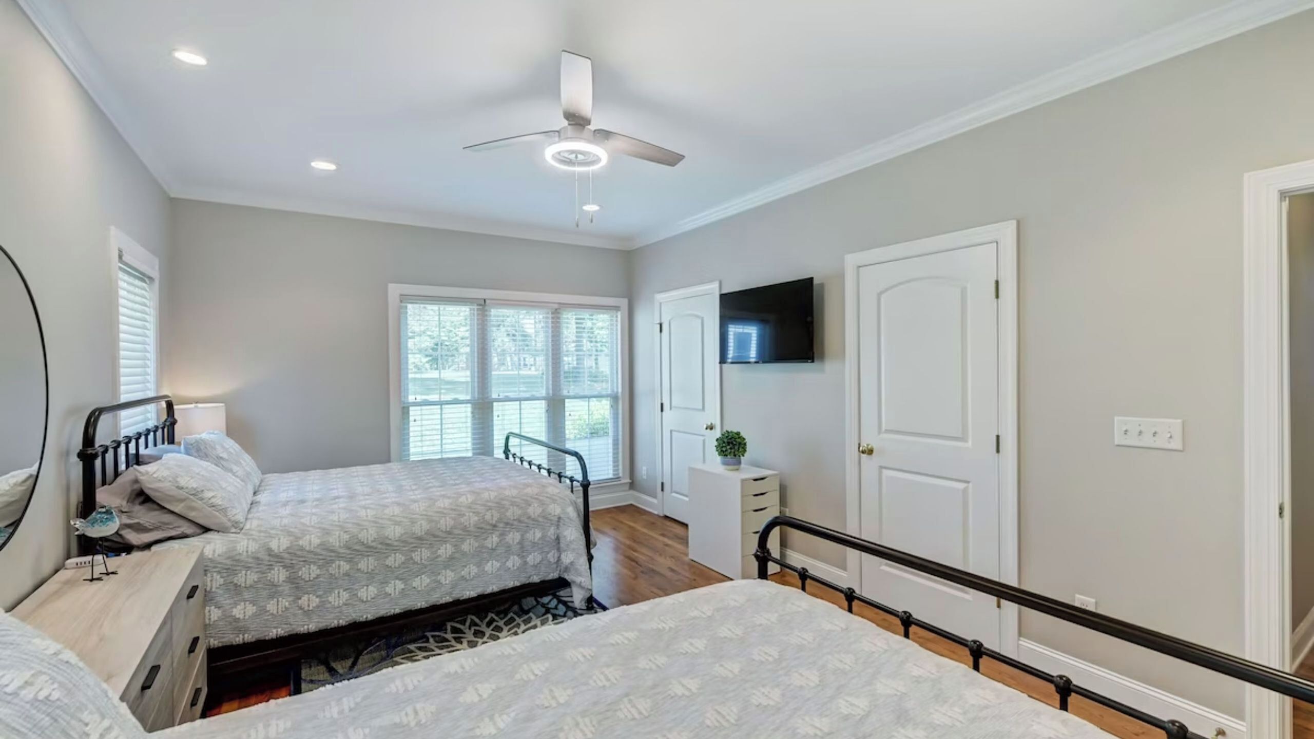 A bedroom with two beds, a ceiling fan, a TV, and a window with blinds.