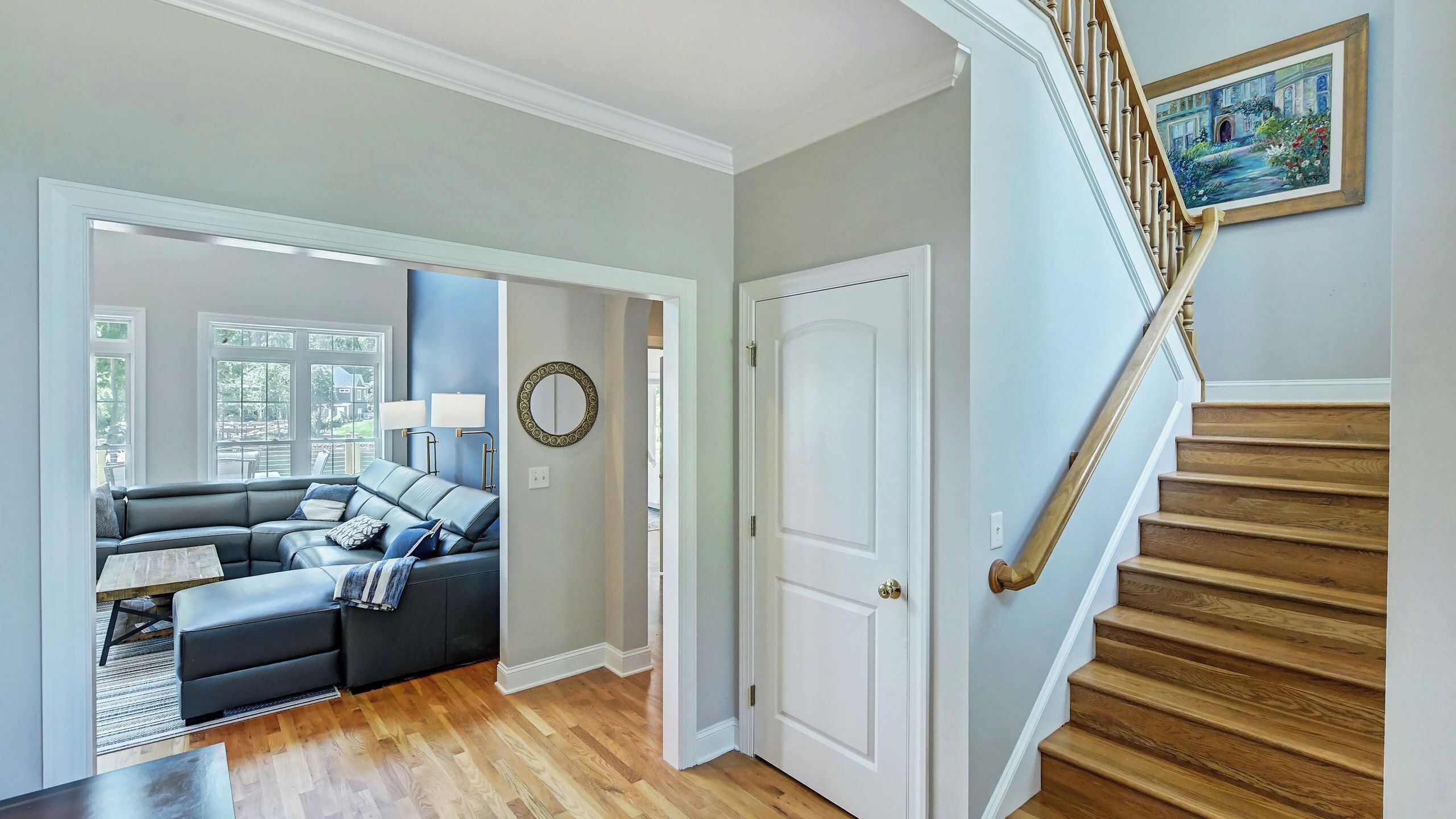 A living room with a sofa, a dining table, and a staircase with a painting.
