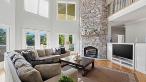 A spacious living room with a stone fireplace, a large window, and a television. - Lakefront 6bdr, Priv Dock, Game Room, Firepit Jake's Lake House by Avantstay (Denver)