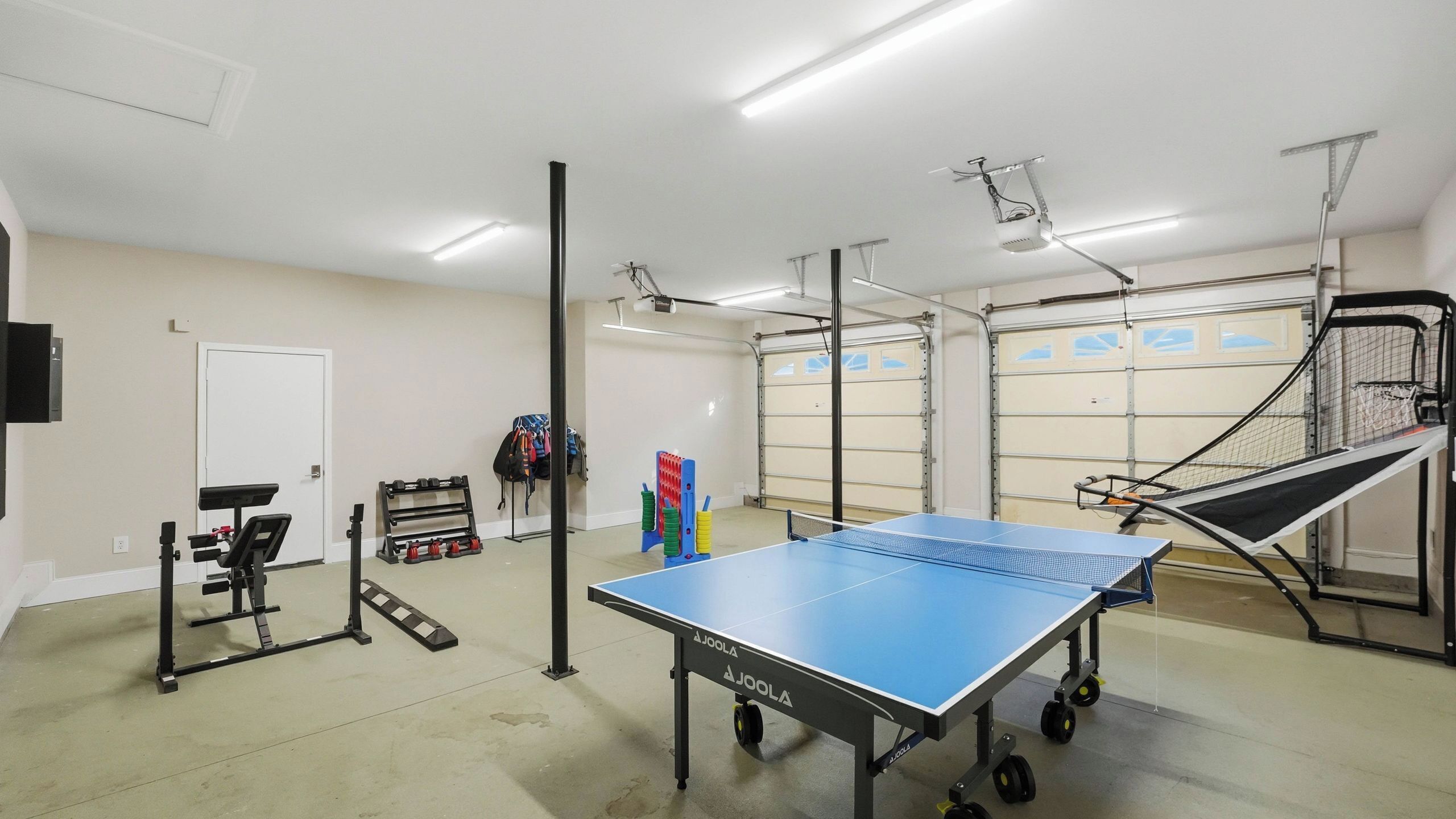 A gym with a ping pong table, exercise equipment, and a basketball hoop.