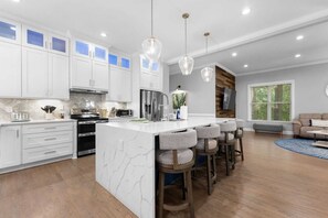 A modern kitchen with white cabinets, a marble island, and bar stools. - Laid Back Lake Life by Avantstay Waterfront View (Mooresville)
