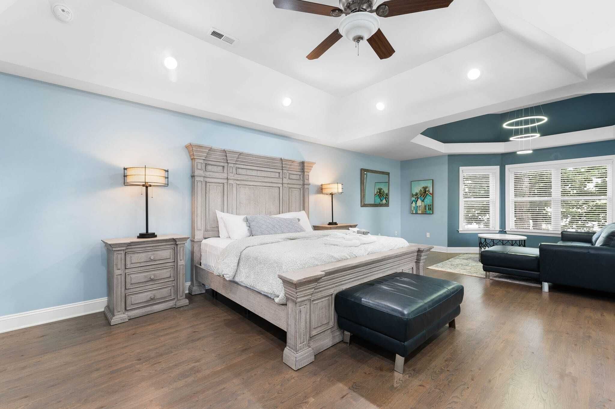 A bedroom with a large bed, two bedside tables, a ceiling fan, and a window with blinds.