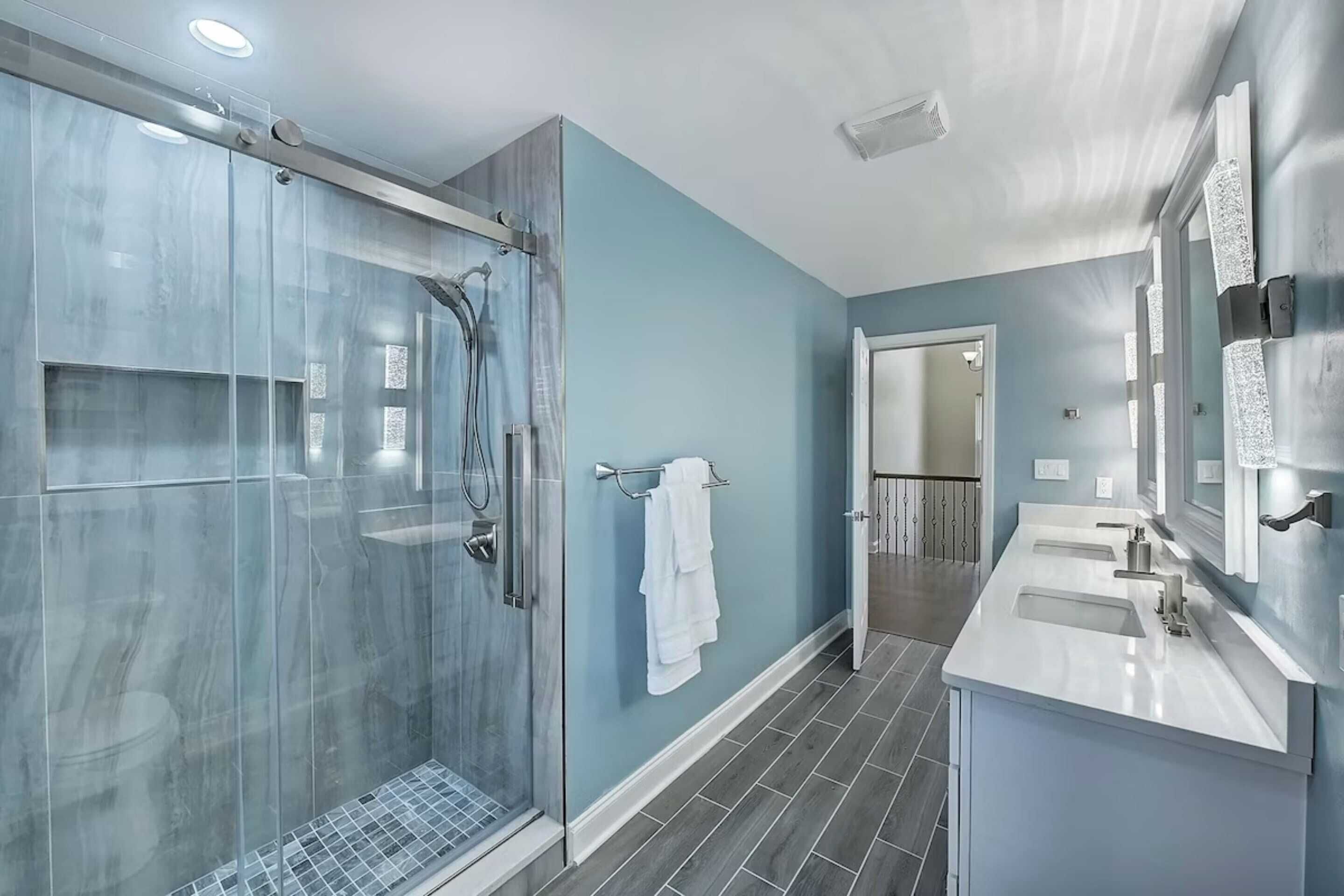Un baño moderno con ducha compartimentada por vidrio, tocador doble y un espejo grande.