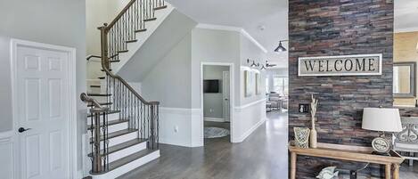 Un intérieur moderne avec un escalier, un panneau d’accueil et un mur d’accent en pierre.