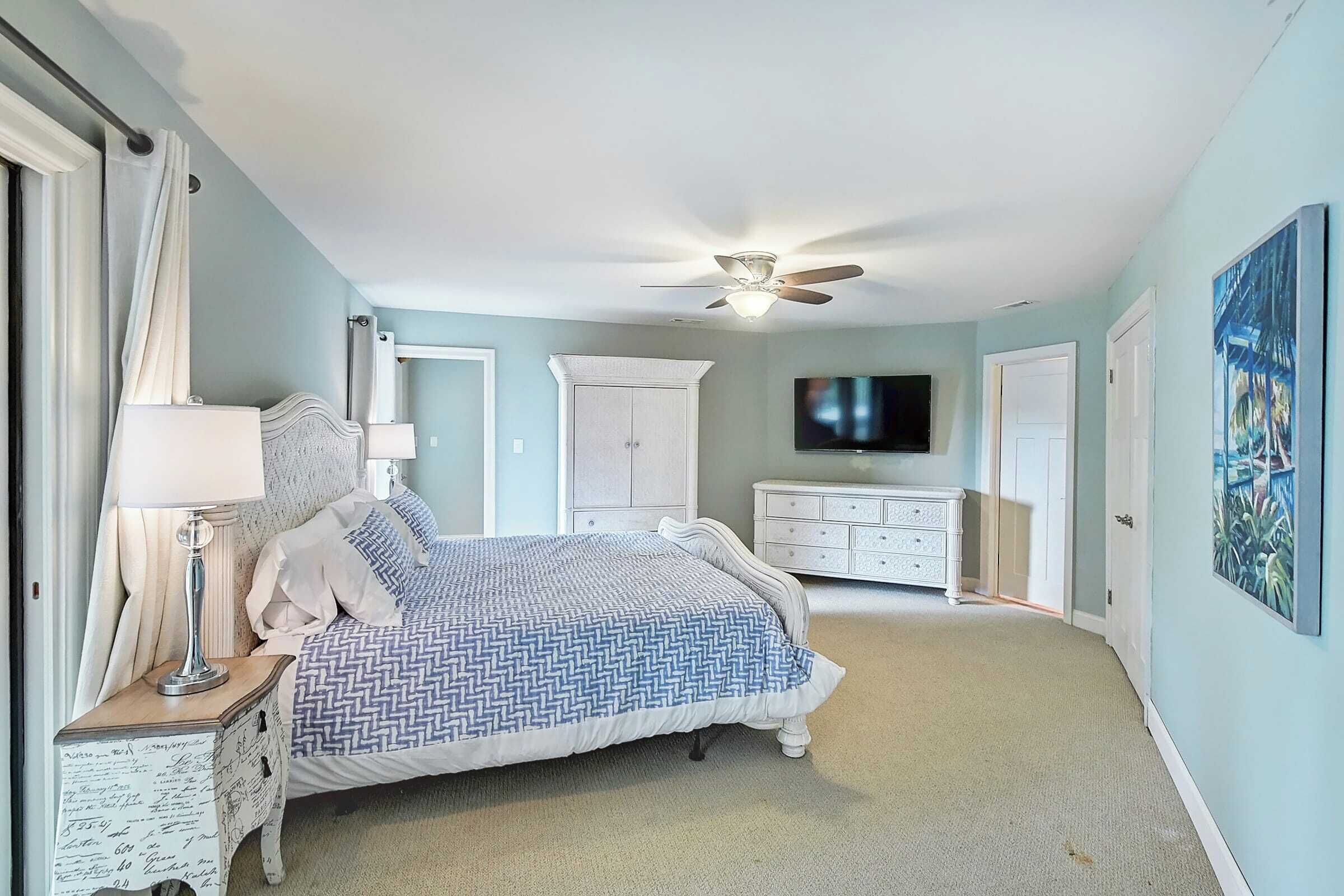 A bedroom with a bed, nightstands, a dresser, a ceiling fan, a television, and a door.