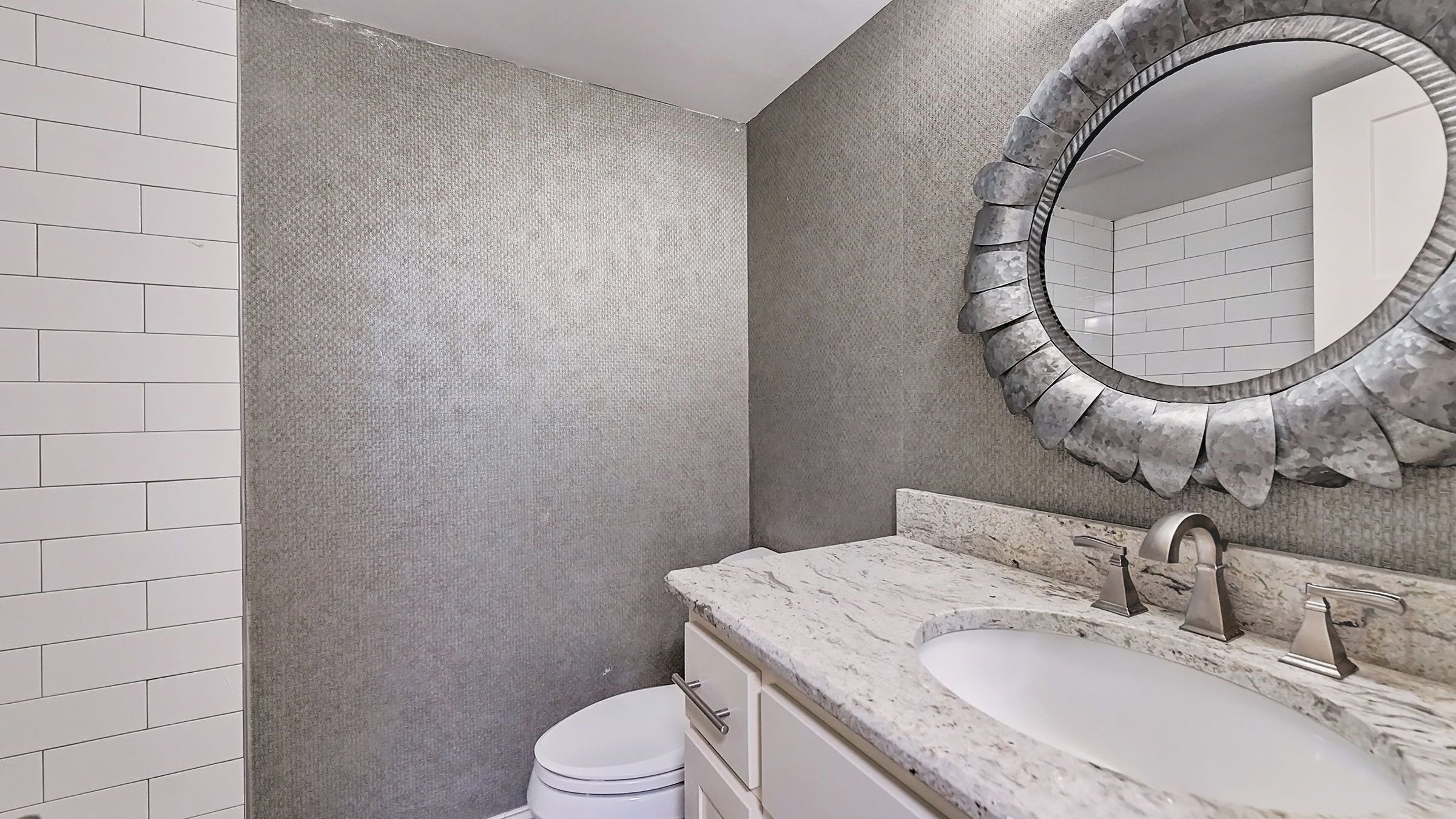 A bathroom with a white toilet, a sink with a marble countertop, and a large mirror with a stone frame.