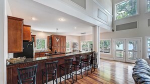 A spacious kitchen with wooden cabinets, a central island with bar stools, and large windows offering views of the outdoors.