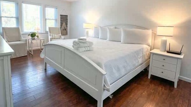A bedroom with a white bed, bedside tables, a chair, and a lamp. - Golf Cart Private pool Bay and Beach Access Pet Friendly (St. George Island)