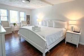 Ein Schlafzimmer mit einem weißen Bett, Nachttischen, einem Sessel und einer Lampe.