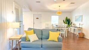 A living room with a blue sofa, yellow cushions, a wooden side table, and a hanging light fixture. - Golf Cart Private pool Bay and Beach Access Pet Friendly (St. George Island)