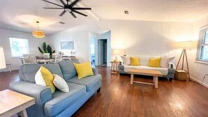 A spacious living room with a blue sofa, a wooden coffee table, and a yellow lamp. - Golf Cart Private pool Bay and Beach Access Pet Friendly (St. George Island)
