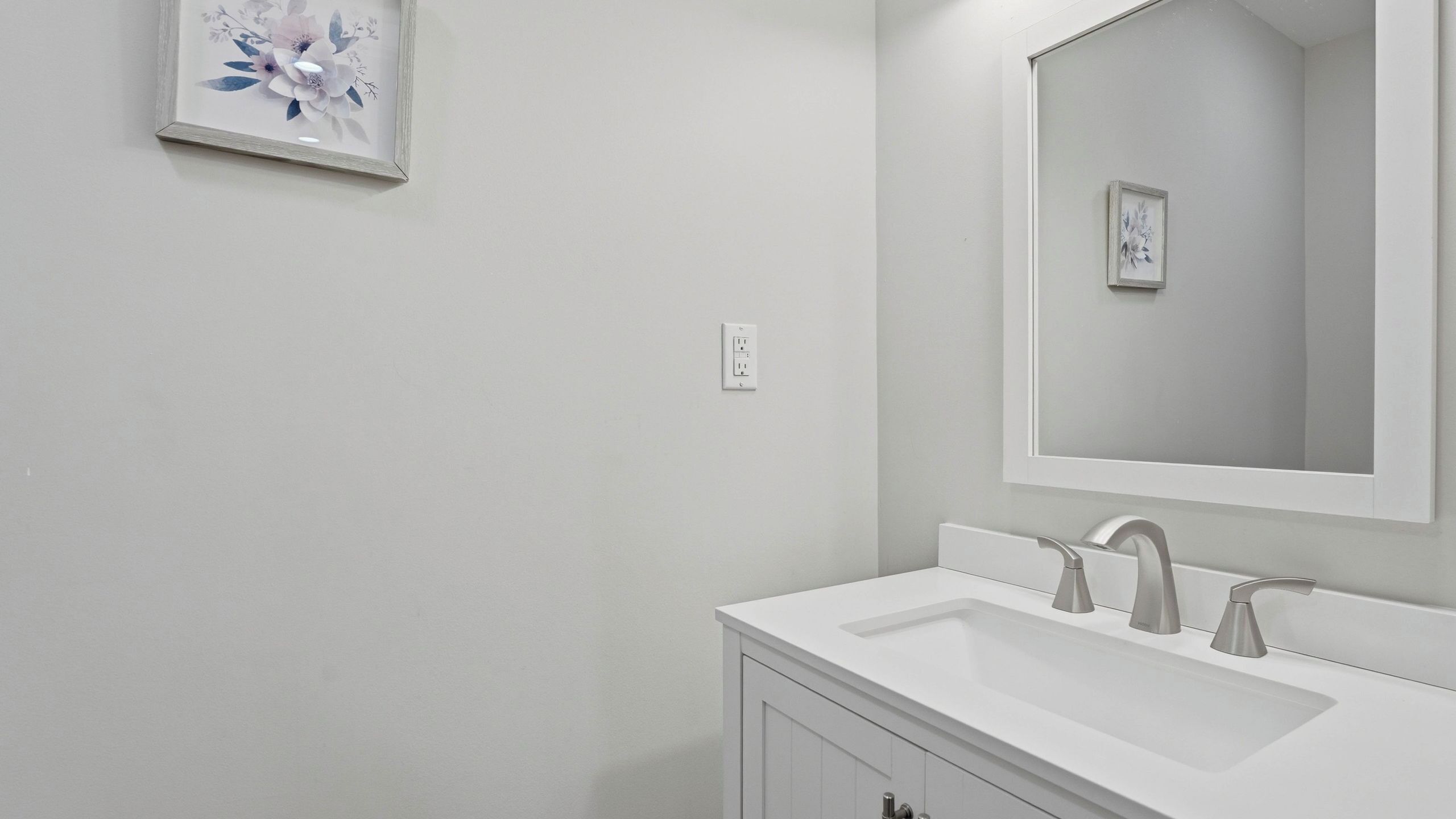 A bathroom with a white sink, a mirror, and a floral artwork on the wall.